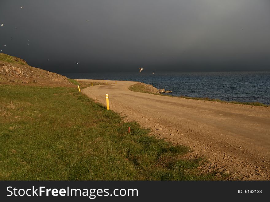 A road partially lit by the sun with a dramatic background of stormy clouds. A road partially lit by the sun with a dramatic background of stormy clouds.