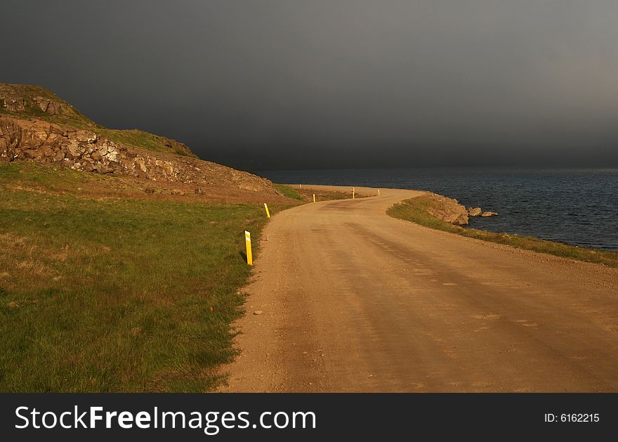 A road partially lit by the sun with a dramatic background of stormy clouds. A road partially lit by the sun with a dramatic background of stormy clouds.