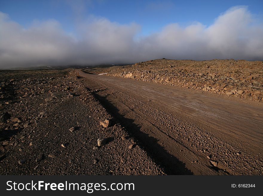 A dirt road running through a stone desert lit by the setting sun. A dirt road running through a stone desert lit by the setting sun.