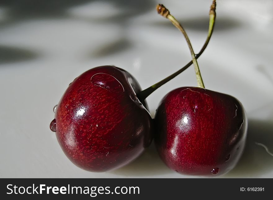 Two small red cherries with fruit stems. Two small red cherries with fruit stems