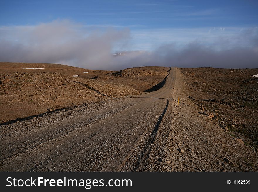 A dirt road running through a stone desert lit by the setting sun. A dirt road running through a stone desert lit by the setting sun.