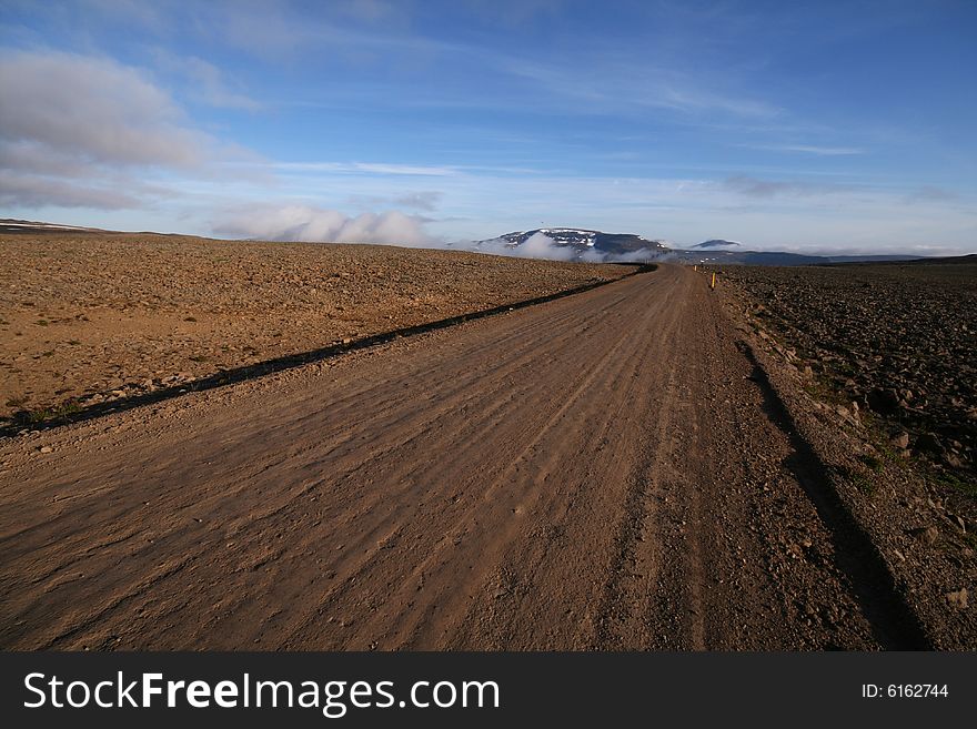 A dirt road running through a stone desert lit by the setting sun. A dirt road running through a stone desert lit by the setting sun.