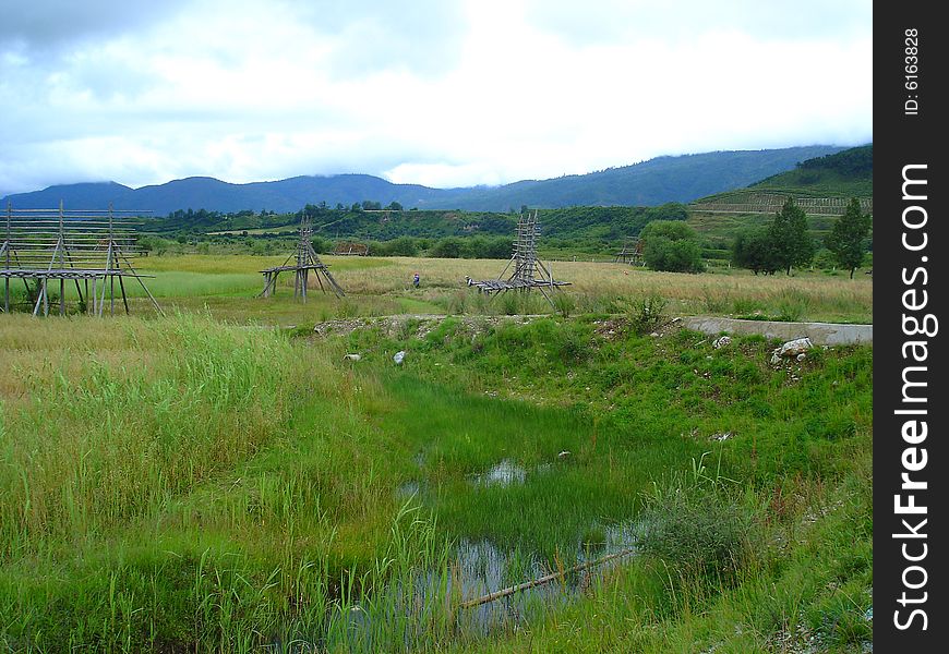 The photo is about Yunan province of China, there is a large field in front of mountains, there are some clouds in the sky. The photo is about Yunan province of China, there is a large field in front of mountains, there are some clouds in the sky.