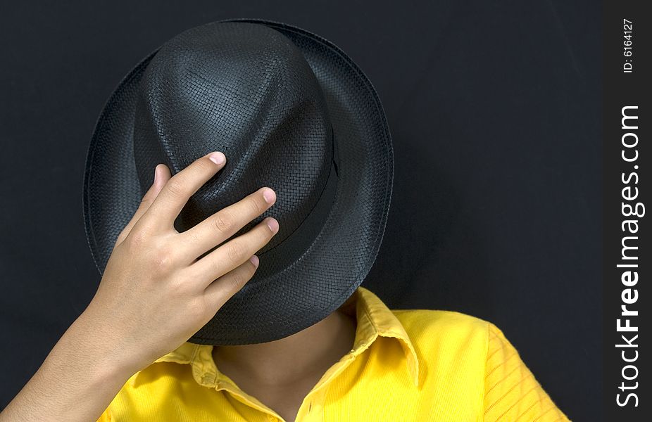 Teenager covers his face with black hat isolated on black background. Teenager covers his face with black hat isolated on black background