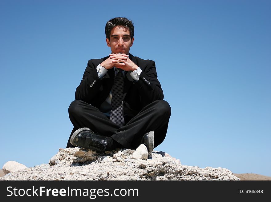 Businessman in black suit sitting on the rocks. Businessman in black suit sitting on the rocks