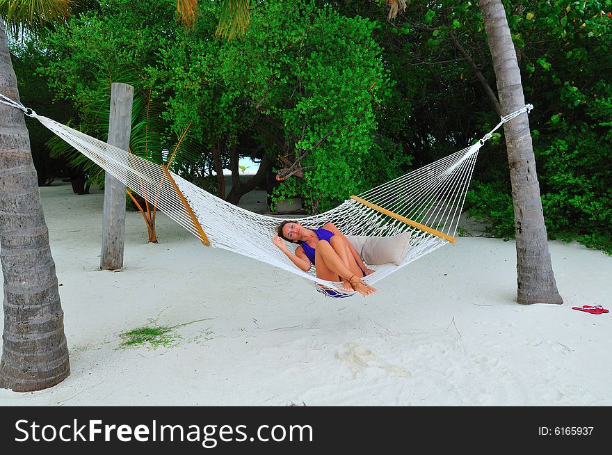 Woman lying on the hammock on a sandy beach in a resort in Maldives