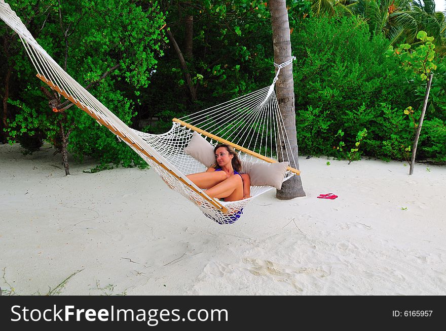 Woman lying on the hammock on a sandy beach in a resort in Maldives