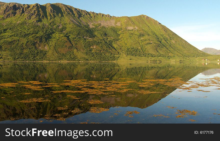 Cape reflecting in a fjord with the midnight's sun, Lofoten islands, Arctic ocean. Cape reflecting in a fjord with the midnight's sun, Lofoten islands, Arctic ocean