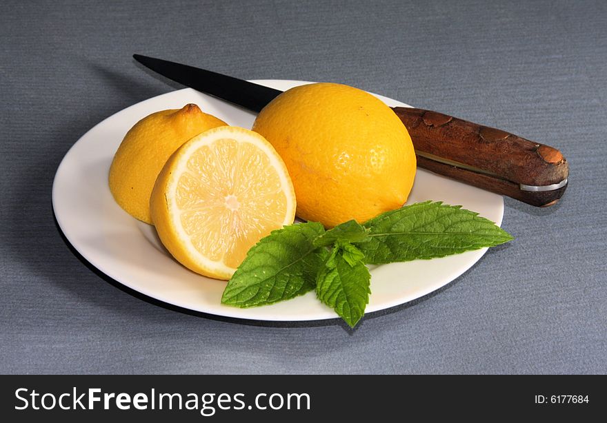 A cut lemon and some mint on a plate waiting for use in the kitchen. A cut lemon and some mint on a plate waiting for use in the kitchen