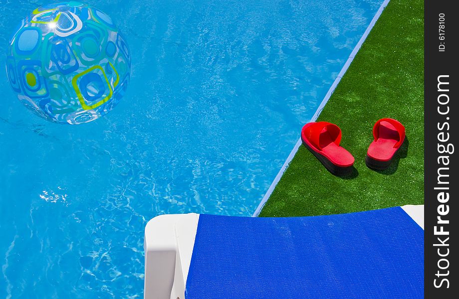 Swimming pool with sun lounger detail, red sandals and water ball. Swimming pool with sun lounger detail, red sandals and water ball