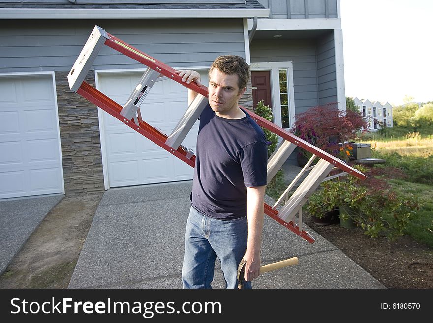 Angry, frowning man standing in front of house holding ladder and hammer. Horizontally framed photo. Angry, frowning man standing in front of house holding ladder and hammer. Horizontally framed photo.