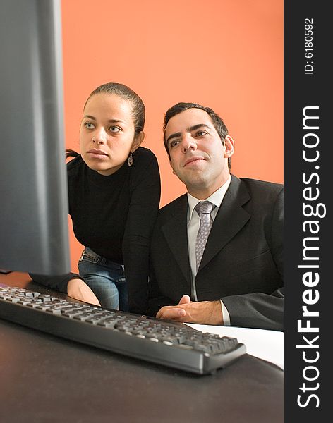 Businessman sits at his desk as his co-worker stands behind him and they look at a computer. Vertically framed photo. Businessman sits at his desk as his co-worker stands behind him and they look at a computer. Vertically framed photo.