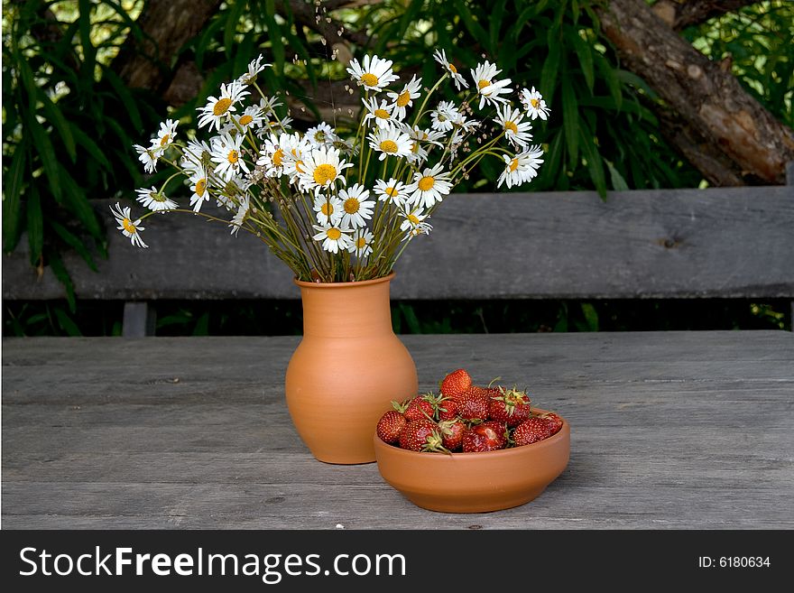 Camomile bouquet and strawberry in a clay bowls. Camomile bouquet and strawberry in a clay bowls