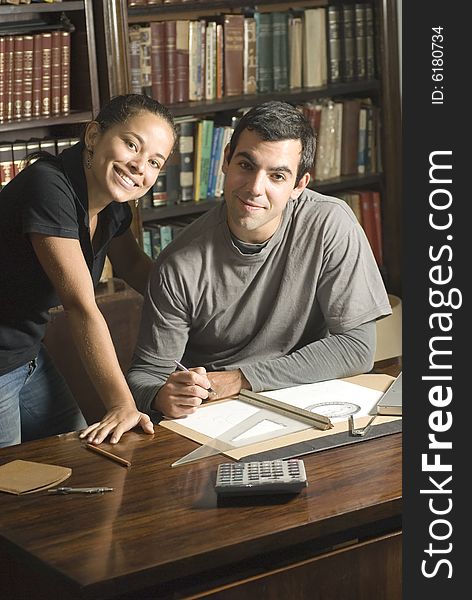 Young, smiling couple study together in an office with many books and a computer. Horizontally framed photo. Young, smiling couple study together in an office with many books and a computer. Horizontally framed photo.