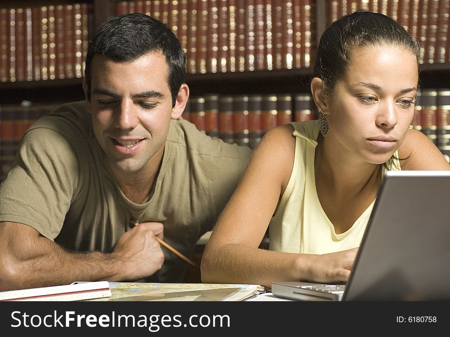 Young couple study together in an office with many books and a computer. Horizontally framed photo. Young couple study together in an office with many books and a computer. Horizontally framed photo.