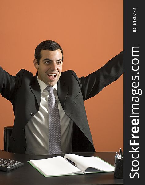 Smiling businessman seated at his computer throwing his arms up in jubilation. Vertically framed photo. Smiling businessman seated at his computer throwing his arms up in jubilation. Vertically framed photo.