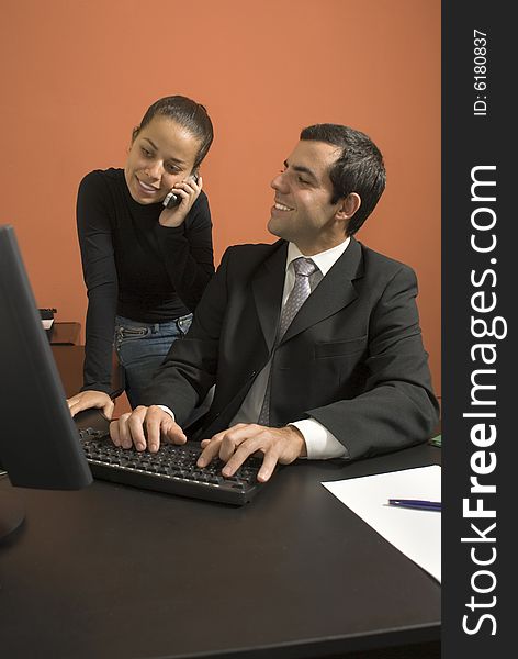 Businessman at his computer looks at his employee as she talks on a cell phone. Vertically framed photo. Businessman at his computer looks at his employee as she talks on a cell phone. Vertically framed photo.