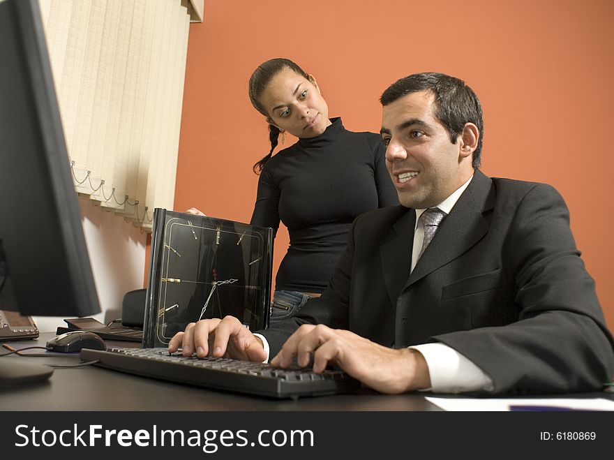 Businessman sits at his desk and looks at his computer while his co-worker stands up looking at him. Vertically framed photo. Businessman sits at his desk and looks at his computer while his co-worker stands up looking at him. Vertically framed photo.