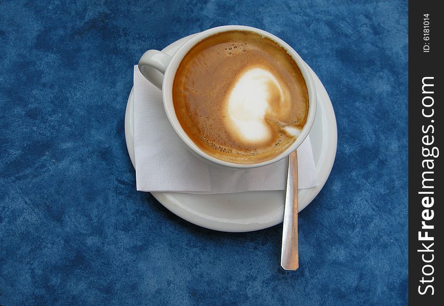 A delicious fresh hot Italian cappuccino in white cup shown fromt top on blue background