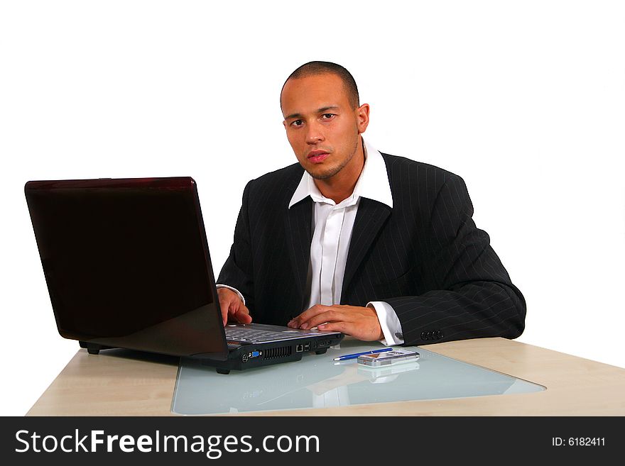 A young businessman sitting by desk at office working on the laptop with cellphone on the table. Isolated over white. A young businessman sitting by desk at office working on the laptop with cellphone on the table. Isolated over white.