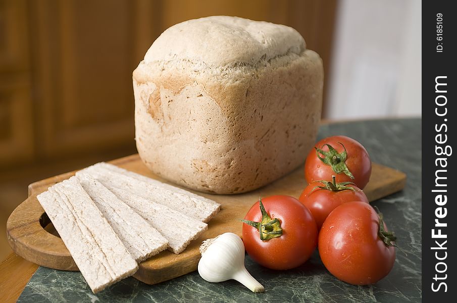 Bread in a breadbord with tomato and garlic on a green table. Bread in a breadbord with tomato and garlic on a green table