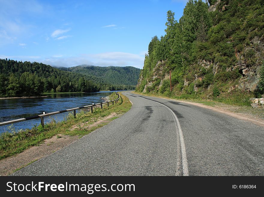 Road going between the river and a rock under the blue sky. Road going between the river and a rock under the blue sky