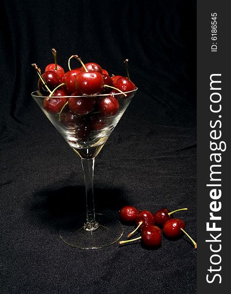 A wine glass full of cherries on a black background. A wine glass full of cherries on a black background.