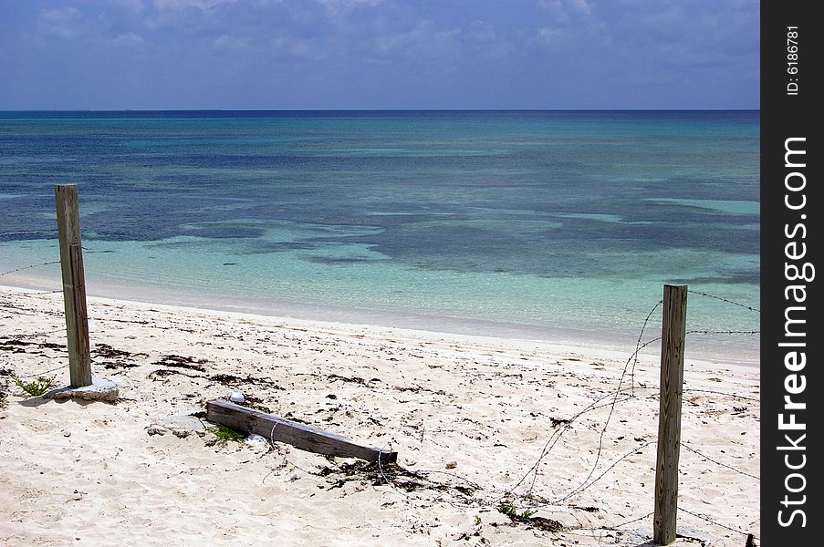 The broken fence gives you access to an empty beach with unspoiled crystal clean Caribbean sea water on Grand Turk island, Turks & Caicos.