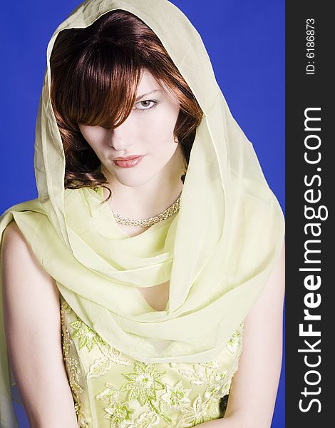 Beautiful young woman wearing green dress with a scarf around her head against a blue back ground. Beautiful young woman wearing green dress with a scarf around her head against a blue back ground