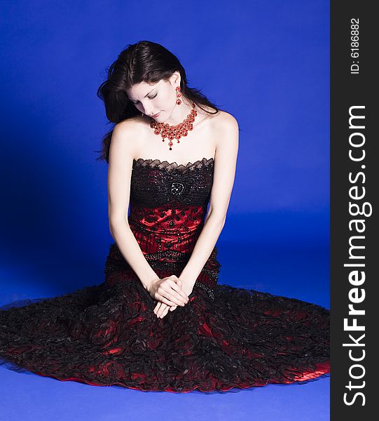 Beautiful young woman wearing red sleeve less evening gown, posing in front of a blue back ground. Beautiful young woman wearing red sleeve less evening gown, posing in front of a blue back ground