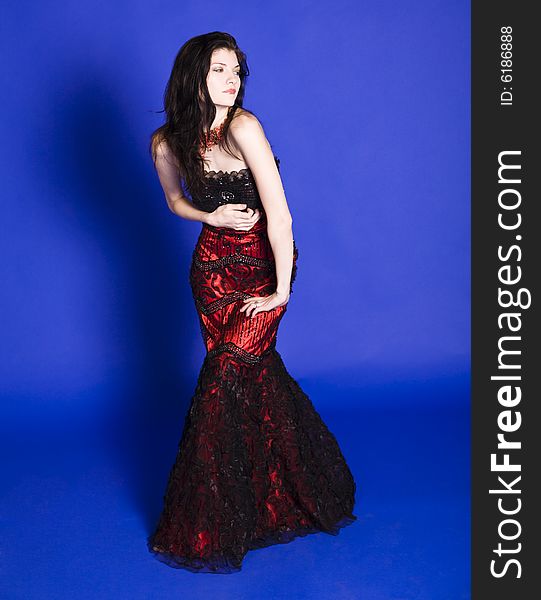 Beautiful young woman wearing red sleeve less evening gown, posing in front of a blue back ground. Beautiful young woman wearing red sleeve less evening gown, posing in front of a blue back ground