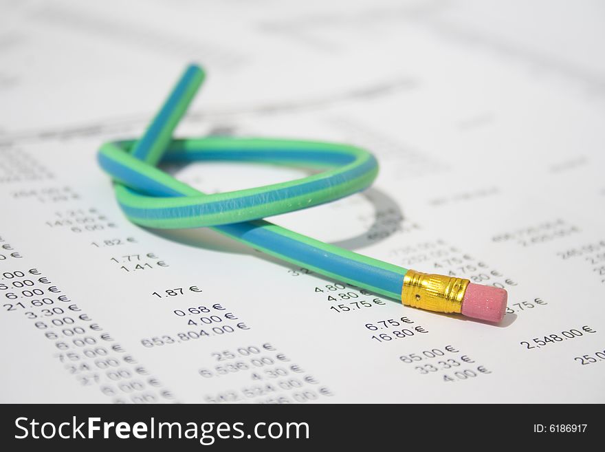 A green and blue striped rubber pencil tied in knot sitting on accounting printout. A green and blue striped rubber pencil tied in knot sitting on accounting printout