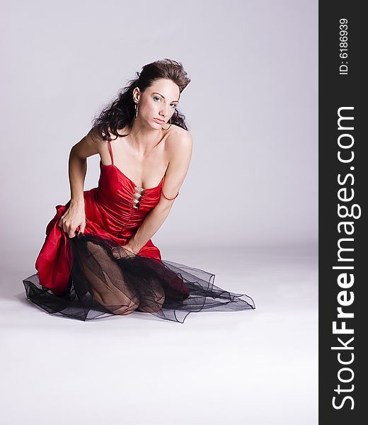 Beautiful young woman with long brunette hair wearing red evening gown sitting on the floor. Beautiful young woman with long brunette hair wearing red evening gown sitting on the floor