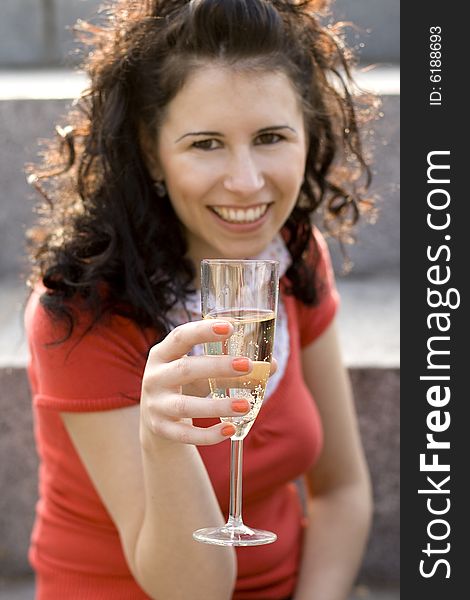 Outdoor portrait of smiling girl with champagne glass, focus on glass