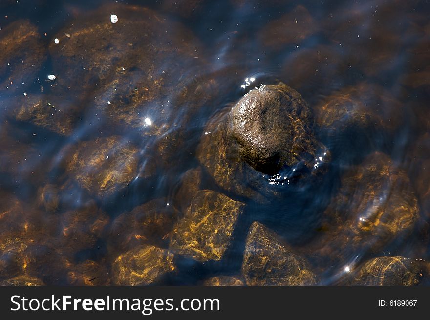 Wet rock sticking out above the surface of the water surrounded by other stones