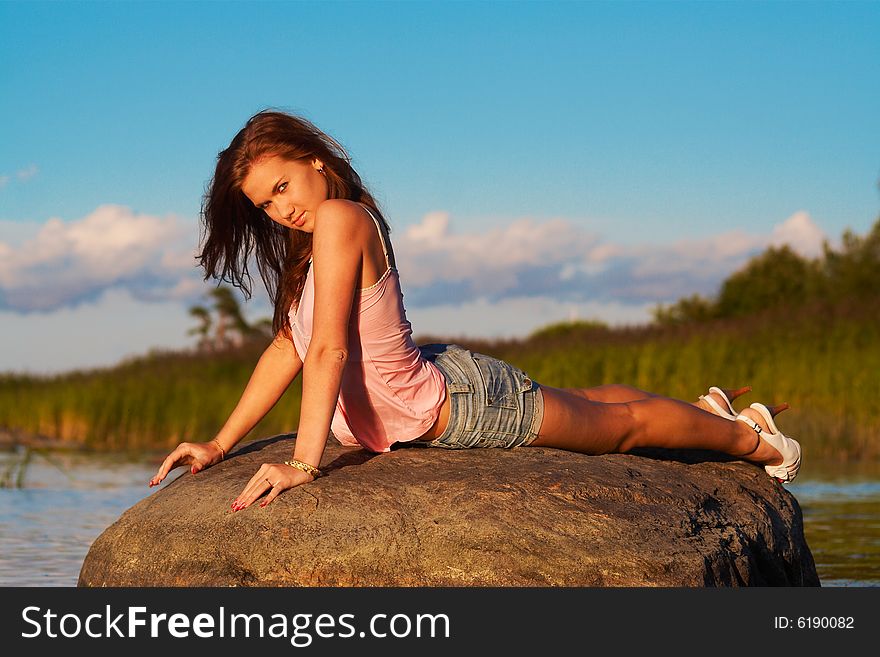 Teenage girl laying on a stone in light of the evening sun