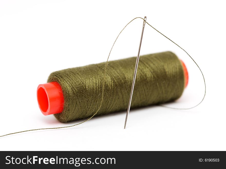 Spool of olive green thread and needle on white background.