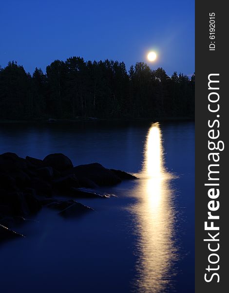 Moon rising and reflecting in the still water of a lake