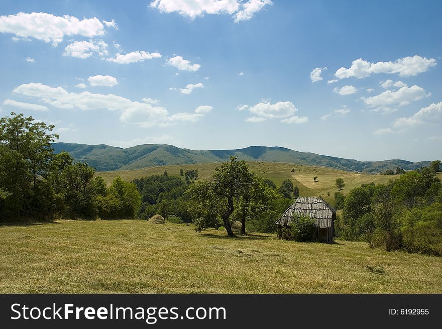 Old style wooden rustic house with an old tree in front with hills and mountains in background. Old style wooden rustic house with an old tree in front with hills and mountains in background