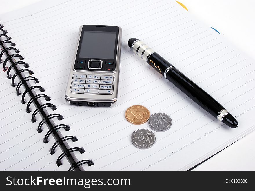 Pen,cellphone,coins on notebook , isolated in white background. Pen,cellphone,coins on notebook , isolated in white background.