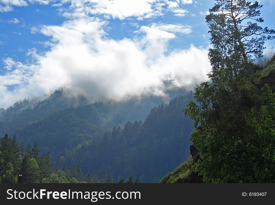 Woody mountains partially hidden in clouds under the blue sky. Woody mountains partially hidden in clouds under the blue sky