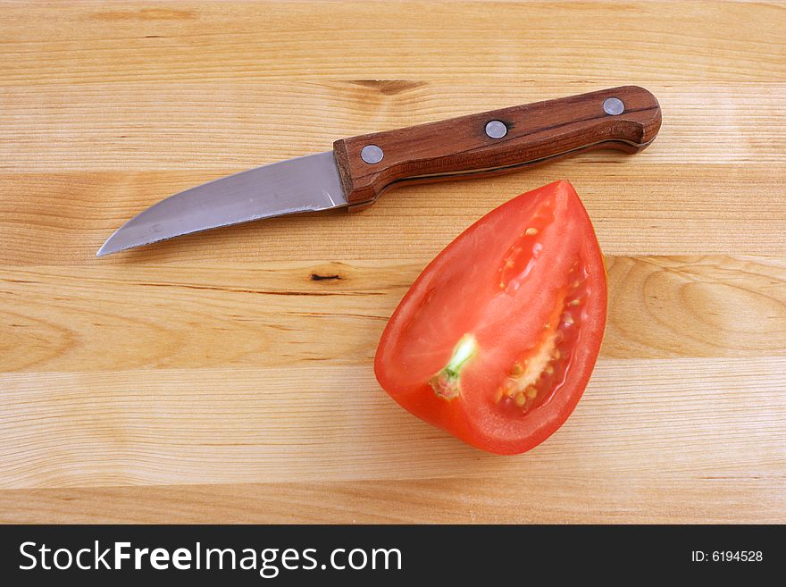 Fresh tomato with knife on kitchen board