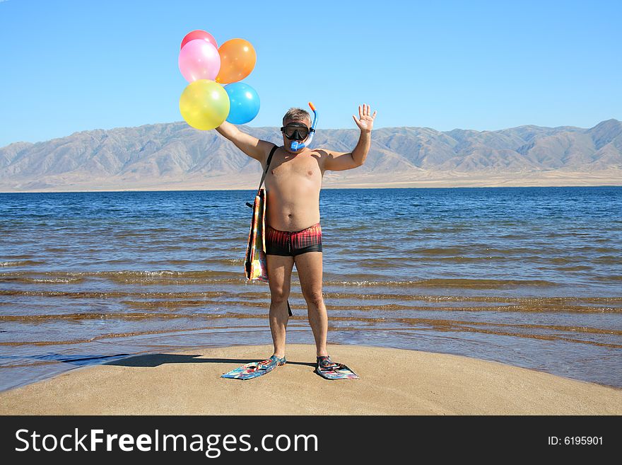 Man with mask, flippers and balloons is salutation  on the beach