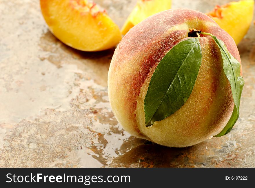 Whole and sliced fresh picked peach on a stone counter.