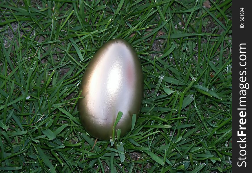 A golden egg in bright green rye grass. A golden egg in bright green rye grass