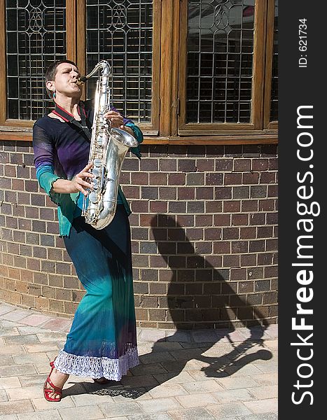 Woman playing saxophone outside with shadow to her left in front of old building. Woman playing saxophone outside with shadow to her left in front of old building.