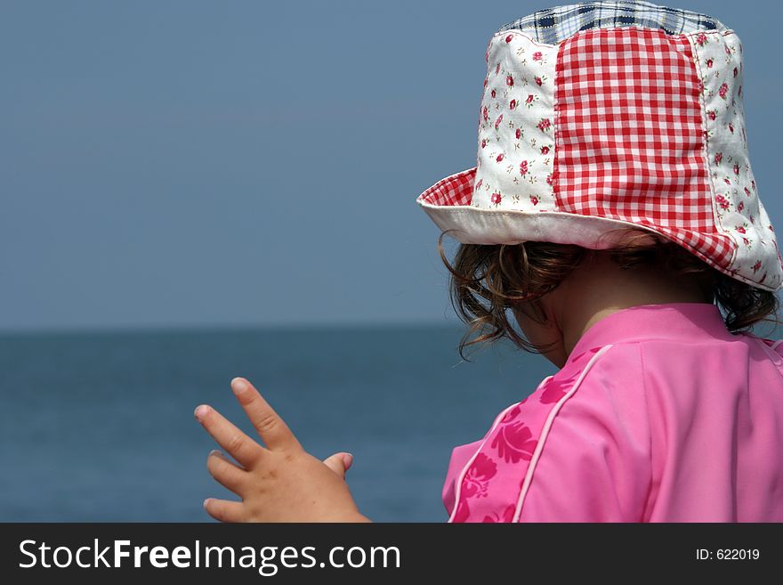 Young girl wearing sun hat looking out to sea, face obscured. Young girl wearing sun hat looking out to sea, face obscured