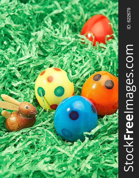 Wooden easter bunny with four coloured easter eggs in green grass