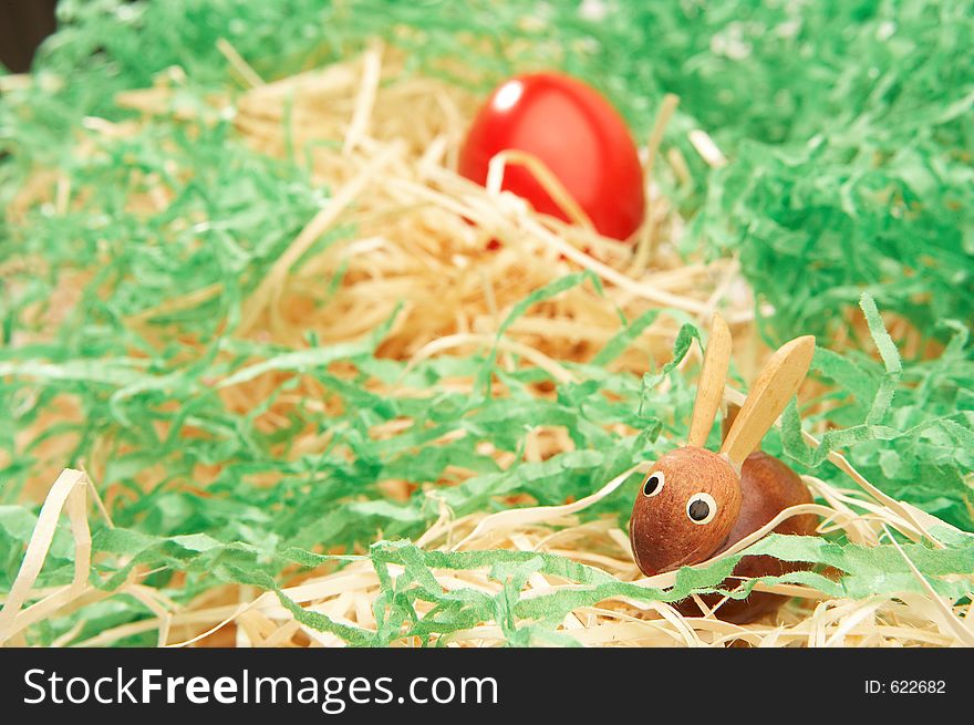 Wooden easter bunny with red easter egg in green grass