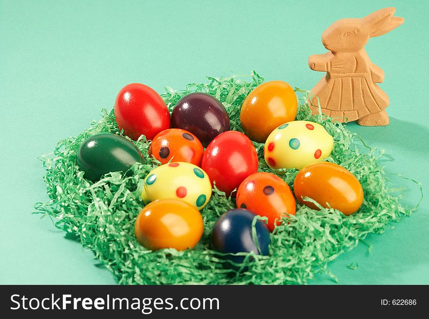 Coloured easter eggs in green grass with ceramic easter bunny on green background